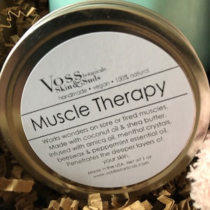 May include: A silver tin with a white label that reads "Voss Skin & Suds handmade vegan 100% natural Muscle Therapy". The label also includes a description of the product's ingredients and benefits. The tin is 1 ounce and made in the USA.