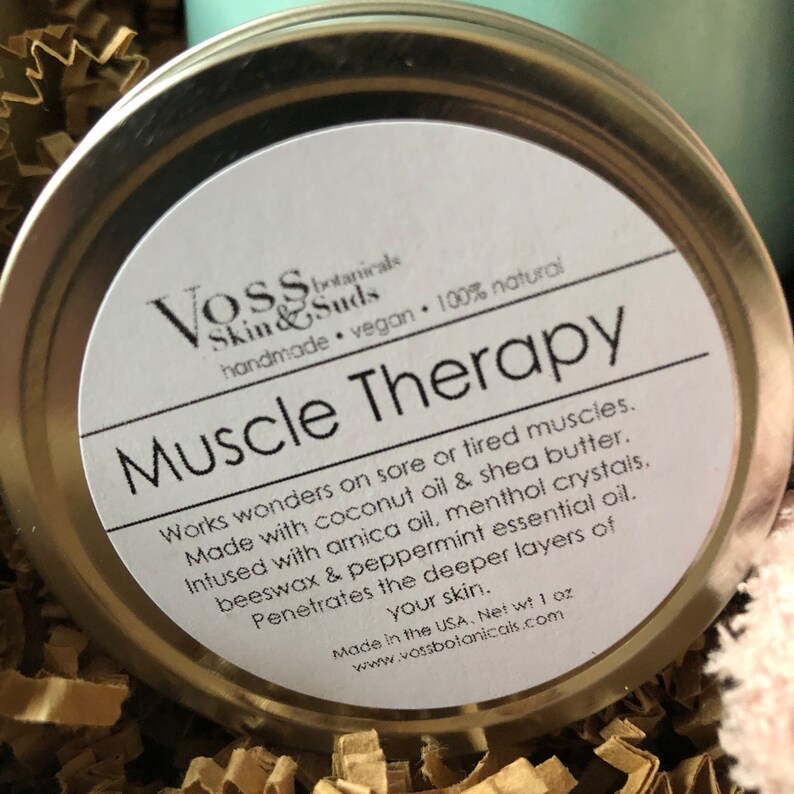 May include: A silver tin with a white label that reads "Voss Skin & Suds handmade vegan 100% natural Muscle Therapy". The label also includes a description of the product's ingredients and benefits. The tin is 1 ounce and made in the USA.