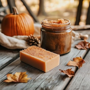 May include: A close-up of a brown sugar scrub in a glass jar, a bar of soap with a brown sugar topping, and fall-themed decorations like a pumpkin and leaves.