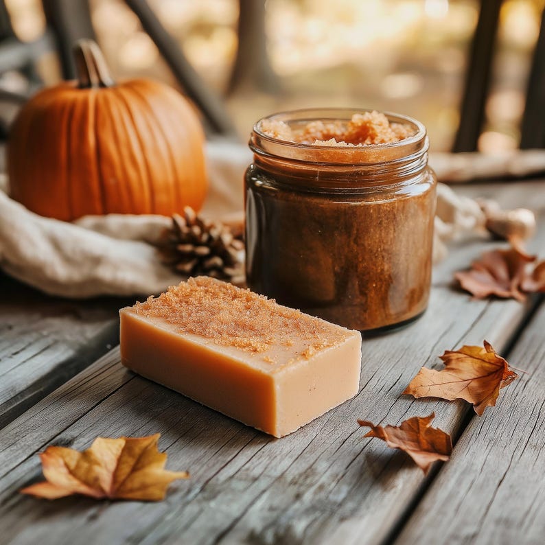 May include: A close-up of a brown sugar scrub in a glass jar, a bar of soap with a brown sugar topping, and fall-themed decorations like a pumpkin and leaves.
