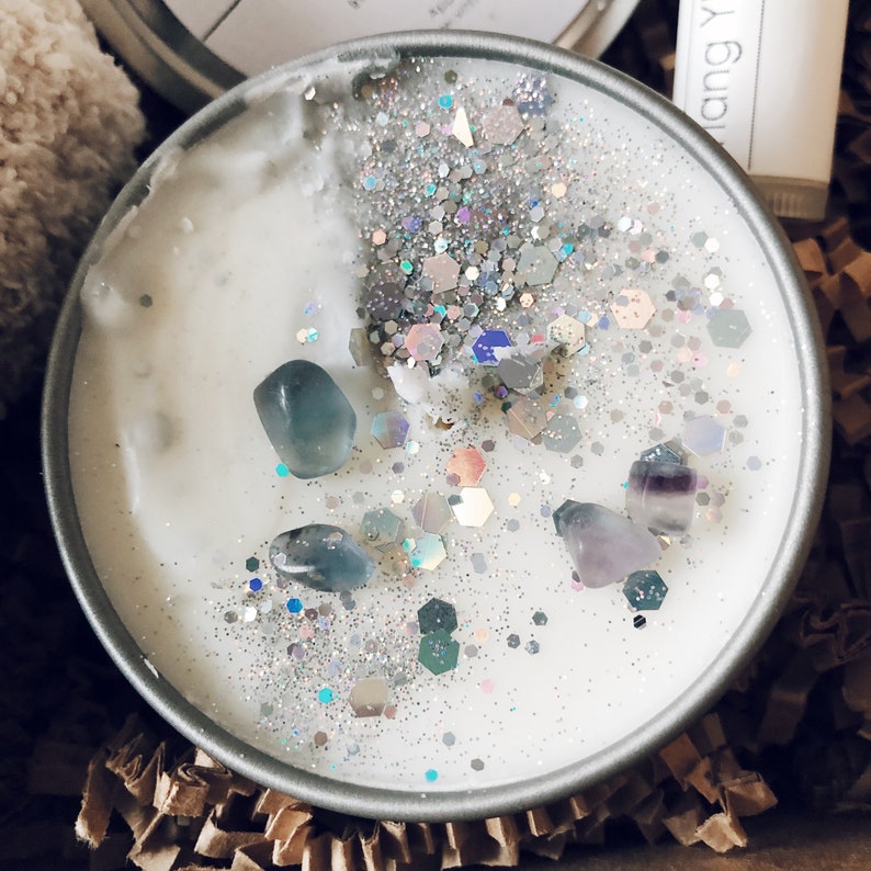 May include: A white candle with silver glitter and blue and purple crystals embedded in the wax.