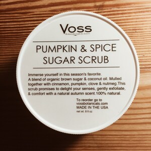 May include: White jar with a black label that reads "Voss Botanicals Bath & Shower Pumpkin & Spice Sugar Scrub". The label also includes the text "Immerse yourself in this season's favorite. A blend of organic brown sugar & coconut oil. Mulled together with cinnamon, pumpkin, clove & nutmeg. This scrub promises to delight your senses, gently exfoliate, & comfort with a natural autumn scent. 100% natural. To reorder go to vossbotanicals.com MADE IN THE USA net wt. 8 fl oz".