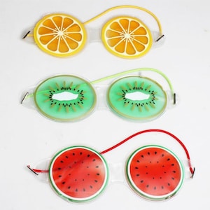 May include: Three pairs of eye masks with fruit designs. The masks are made of clear gel with a printed design of a slice of orange, kiwi, and watermelon. Each mask has an elastic band for wearing.