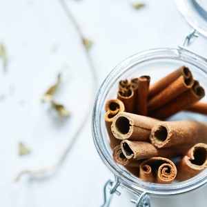 May include: A glass jar filled with cinnamon sticks. The jar has a metal clasp closure and is sitting on a white surface.