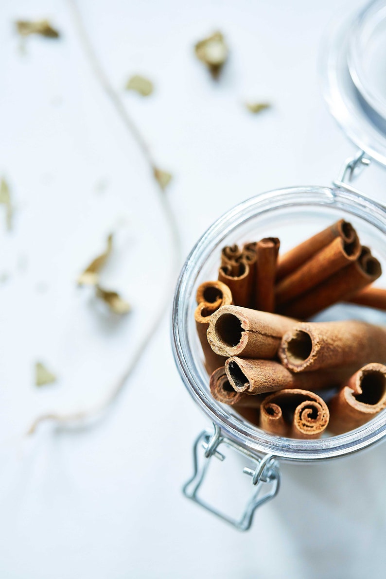 May include: A glass jar filled with cinnamon sticks. The jar has a metal clasp closure and is sitting on a white surface.