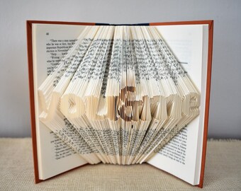 May include: A book with the words "You & Me" folded into the pages. The book is open and the pages are fanned out to create a 3D effect.