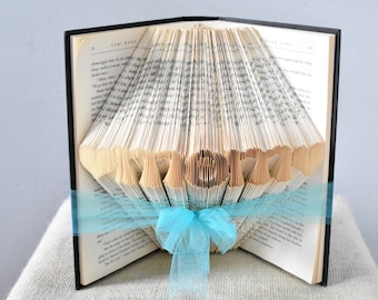 May include: A book with the pages folded into the shape of the word "LOVE" decorated with a blue ribbon.