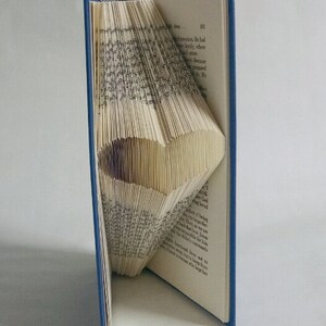 May include: A book folded into a heart shape. The book is open and the pages are folded in a way that creates a three-dimensional heart. The book is blue on the outside.