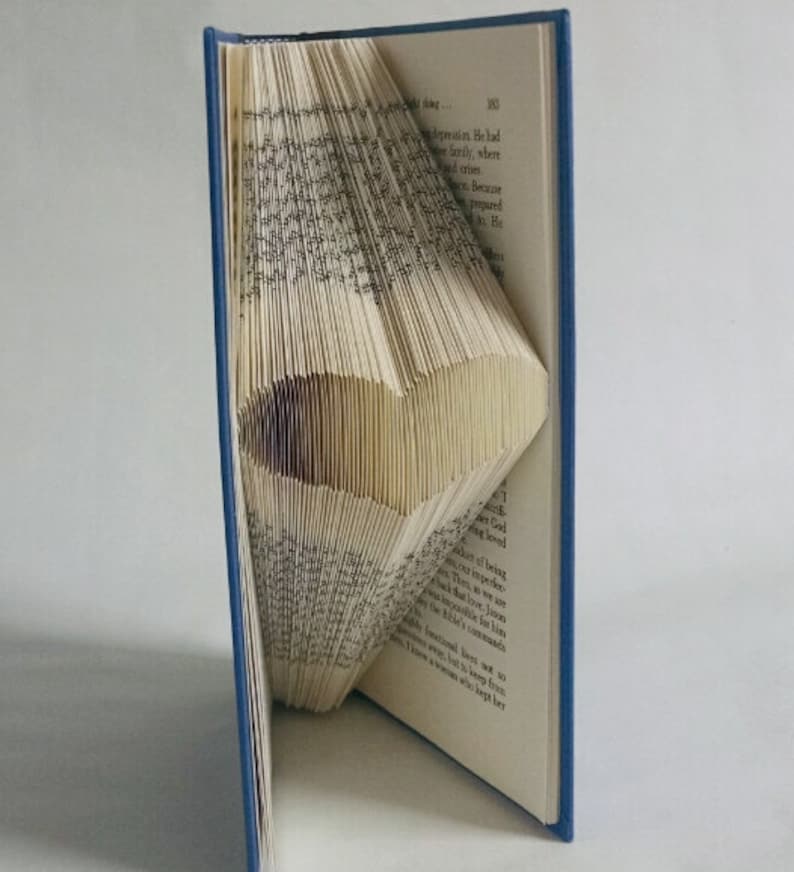 May include: A book folded into a heart shape. The book is open and the pages are folded in a way that creates a three-dimensional heart. The book is blue on the outside.