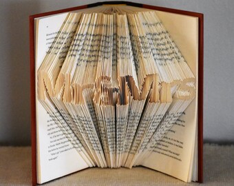 May include: A book with the words "Mr & Mrs" folded into the pages. The book is open and the pages are fanned out to create a 3D effect.