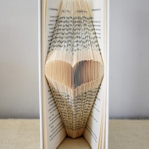May include: A book with pages folded into a heart shape. The book is white with a green spine. The heart is made of the pages of the book.