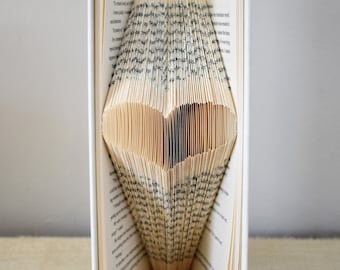 May include: A book with pages folded into a heart shape. The book is white with a green spine. The heart is made of the pages of the book.
