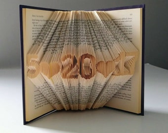 May include: A book with pages folded into the shape of the number "5.20.2021". The book is closed and has a dark blue cover.