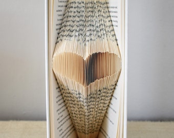 May include: A book with pages folded into a heart shape. The book is white with a green spine. The heart is made of the pages of the book.