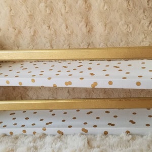 May include: Two-tiered white shelf unit with gold polka dots and gold painted trim. The shelf unit is made of wood and has a rustic look.