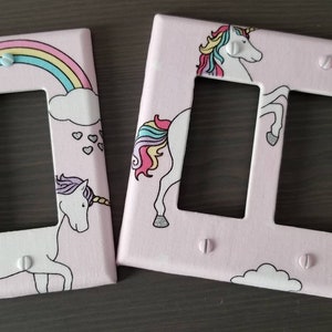 May include: Two pink light switch covers with unicorn and rainbow designs. One cover has a single switch and the other has two switches.