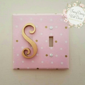 May include: A pink light switch cover with white and gold polka dots. The cover features a gold letter "S" in a decorative script font. The text "Fancy Dancy Wall Decor" is visible in the upper right corner of the image.