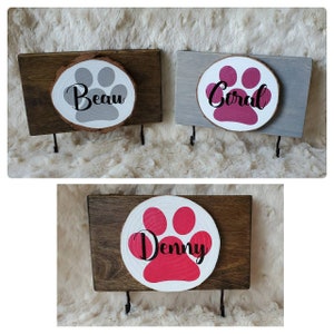 May include: Three wooden key hooks with paw print designs and names "Beau", "Coral", and "Denny". Each hook has two metal hooks for hanging keys or leashes.