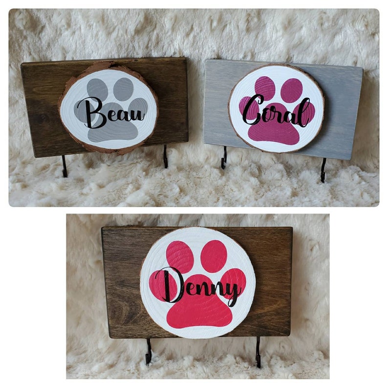 May include: Three wooden key hooks with paw print designs and names "Beau", "Coral", and "Denny". Each hook has two metal hooks for hanging keys or leashes.