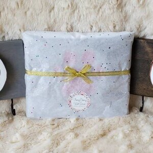 May include: Three wooden pet memorial signs with paw prints and names. The signs are on a white fuzzy surface. The signs are for Wilson, Emily, and a third pet. The signs have hooks on the bottom.