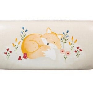 May include: A white oval-shaped glasses case featuring a sleeping fox illustration. The fox is orange with a white belly and tail. The background has a floral design with red, yellow, and blue flowers.