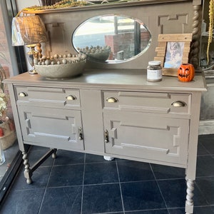 Könnte beinhalten: Ein antiker Anrichte, grau lackiert, mit einem Spiegel und zwei Türen. Die Anrichte hat gedrehte Beine und Messingbeschläge. Die Oberseite der Anrichte hat ein dekoratives Design.