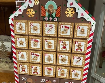 May include: A wooden gingerbread house advent calendar with 24 numbered doors. Each door features a different Christmas-themed image, including gingerbread men, candy canes, and stars. The house is decorated with red and white candy cane stripes, green icing, and white snowflakes.