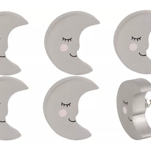 May include: Six gray crescent moon shaped cabinet knobs with a sleeping face and a pink blush. One knob has a screw attached.