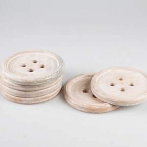 May include: Set of six white wooden coasters with a button design. Each coaster has four holes in the center, resembling a button.