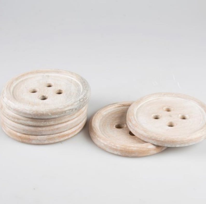 May include: Set of six white wooden coasters with a button design. Each coaster has four holes in the center, resembling a button.