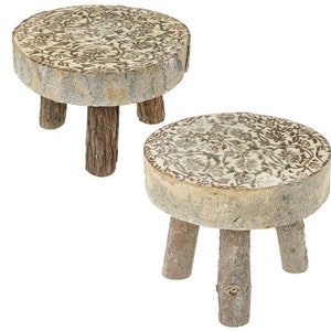 May include: Two wooden stools with a whitewashed finish and a floral design. The stools have three legs each and are made of natural wood.