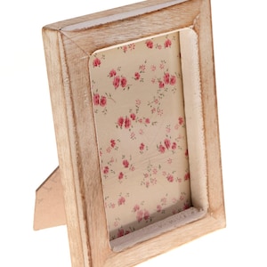 May include: A light wood picture frame with a floral pattern on the inside. The frame has a stand on the back for displaying on a table.