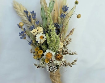 May include: A boutonniere composed of dried flowers and grasses, including purple lavender sprigs, white daisies, yellow billy buttons, and stalks of wheat. The stems are tightly wrapped in natural jute twine, which is tied into a small decorative bow.