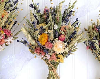 May include: A bouquet of dried flowers featuring purple lavender, yellow strawflowers, pink globe amaranth, and green wheat stalks. The stems are gathered and tied together with a thin brown twine, creating a natural arrangement of dried botanicals.