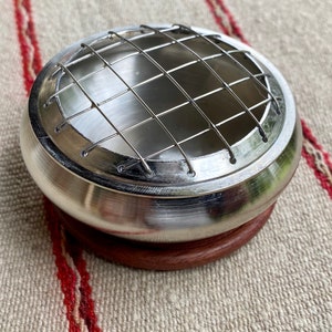 K&ouml;nnte beinhalten: Ein silberner Metall-R&auml;ucherofen mit einem Drahtgitter oben und einem Holzsockel. Der Ofen ist daf&uuml;r ausgelegt, gl&uuml;hende Kohle f&uuml;r R&auml;ucherst&auml;bchen zu halten.