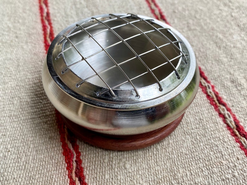 K&ouml;nnte beinhalten: Ein silberner Metall-R&auml;ucherofen mit einem Drahtgitter oben und einem Holzsockel. Der Ofen ist daf&uuml;r ausgelegt, gl&uuml;hende Kohle f&uuml;r R&auml;ucherst&auml;bchen zu halten.