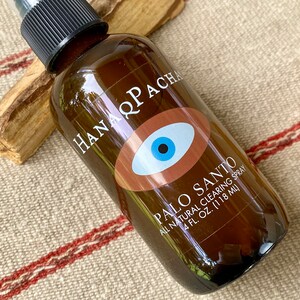 Peut inclure: Une bouteille en verre brun avec un vaporisateur noir et une &eacute;tiquette blanche. L'&eacute;tiquette pr&eacute;sente un &oelig;il brun avec une pupille bleue et le texte "HANA Q PACHA PALO SANTO ALL NATURAL CLEARING SPRAY 4 FL. OZ. (118 ML)"
