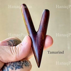 May include: A V-shaped massage tool crafted from dark brown tamarind wood with a smooth, polished finish. The object features two tapered prongs extending from a single pointed base, showcasing the natural grain patterns of the wood throughout.
