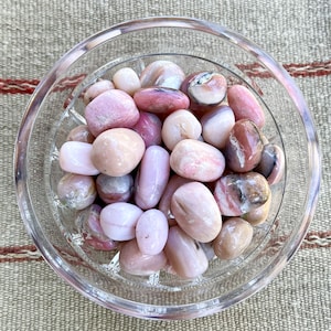 May include: A glass bowl filled with pink and white tumbled stones. The stones are smooth and have a variety of patterns and textures.