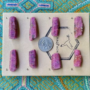 May include: Eight pink ruby crystals arranged in rows on a brown card with numbers 1 through 8 printed next to each crystal. The card also has the word "NARPACH" printed on it.