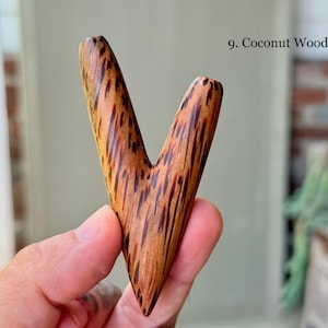 May include: A V-shaped object crafted from coconut wood, featuring a smooth, polished surface with a distinct dark brown and tan speckled grain pattern. The item is labeled as 9. Coconut Wood in the upper right corner of the image.
