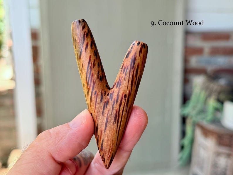 May include: A V-shaped object crafted from coconut wood, featuring a smooth, polished surface with a distinct dark brown and tan speckled grain pattern. The item is labeled as 9. Coconut Wood in the upper right corner of the image.