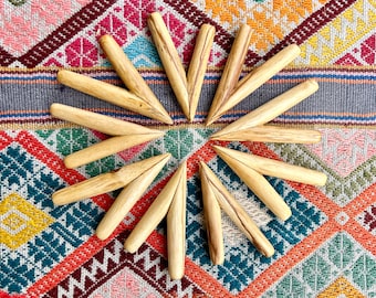 May include: A collection of twelve wooden knitting needles arranged in a circular pattern. The needles are light brown with a pointed end and a rounded top. The background is a colorful textile with geometric patterns in various colors.