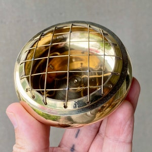 K&ouml;nnte beinhalten: Ein goldfarbener Metall-R&auml;ucherofen mit einem Drahtgitter. Der Ofen ist rund und hat eine glatte, polierte Oberfl&auml;che.