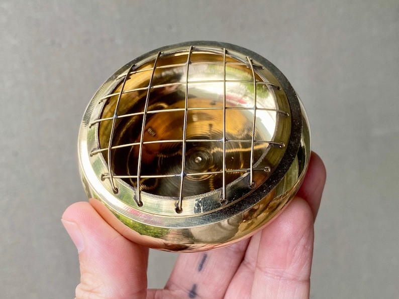 K&ouml;nnte beinhalten: Ein goldfarbener Metall-R&auml;ucherofen mit einem Drahtgitter. Der Ofen ist rund und hat eine glatte, polierte Oberfl&auml;che.