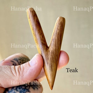 May include: A V-shaped wooden tool with a smooth, polished finish and visible dark brown grain patterns. The object is labeled with the text Teak and features a pointed bottom end with two upward-extending prongs of slightly different lengths.
