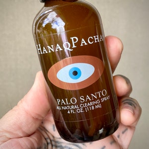 Peut inclure: Une bouteille en verre brun avec une &eacute;tiquette blanche qui dit "HANAQ PACHA" et "PALO SANTO ALL NATURAL CLEARING SPRAY 4 FL. OZ. (118 ML)". L'&eacute;tiquette pr&eacute;sente &eacute;galement un &oelig;il bleu avec une pupille noire &agrave; l'int&eacute;rieur d'un ovale brun.