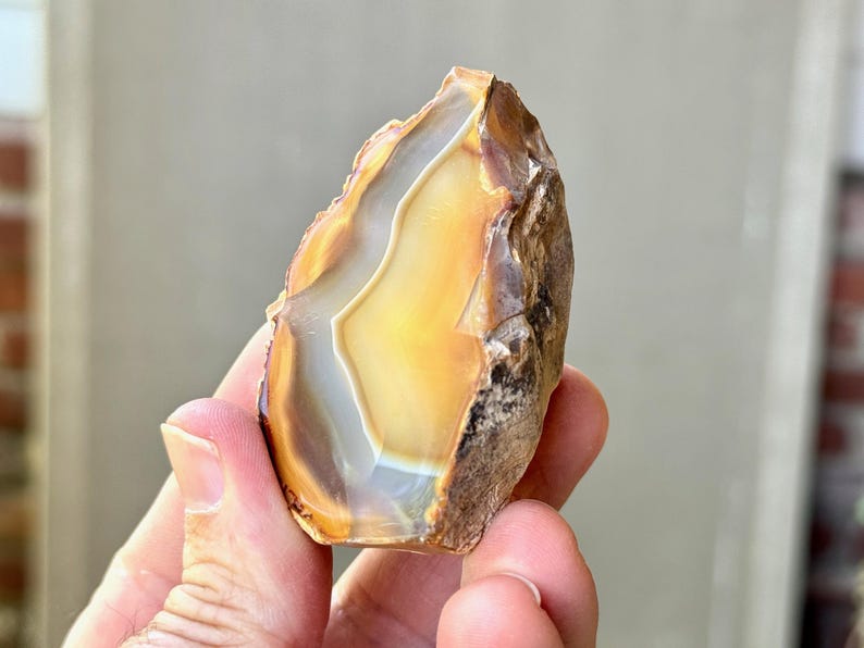 May include: A natural agate stone with a brown, white, and yellow banded pattern. The stone is rough and has a natural, unpolished finish.
