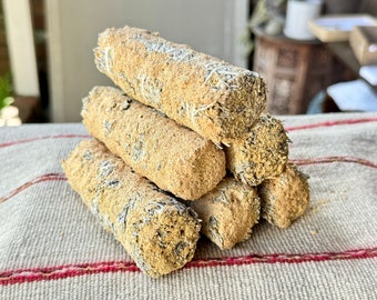 May include: A stack of four beige and white sage smudge sticks, arranged in a pyramid shape, on a striped fabric surface.