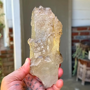 May include: A large, translucent, pale yellow quartz crystal cluster with a rough, textured surface and jagged edges. The mineral specimen features natural formations with varying degrees of clarity and internal fractures throughout the structure.